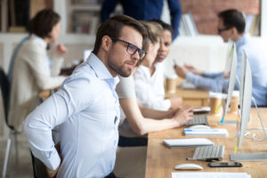 Office employee rubs sore back due to poor office ergonomics.